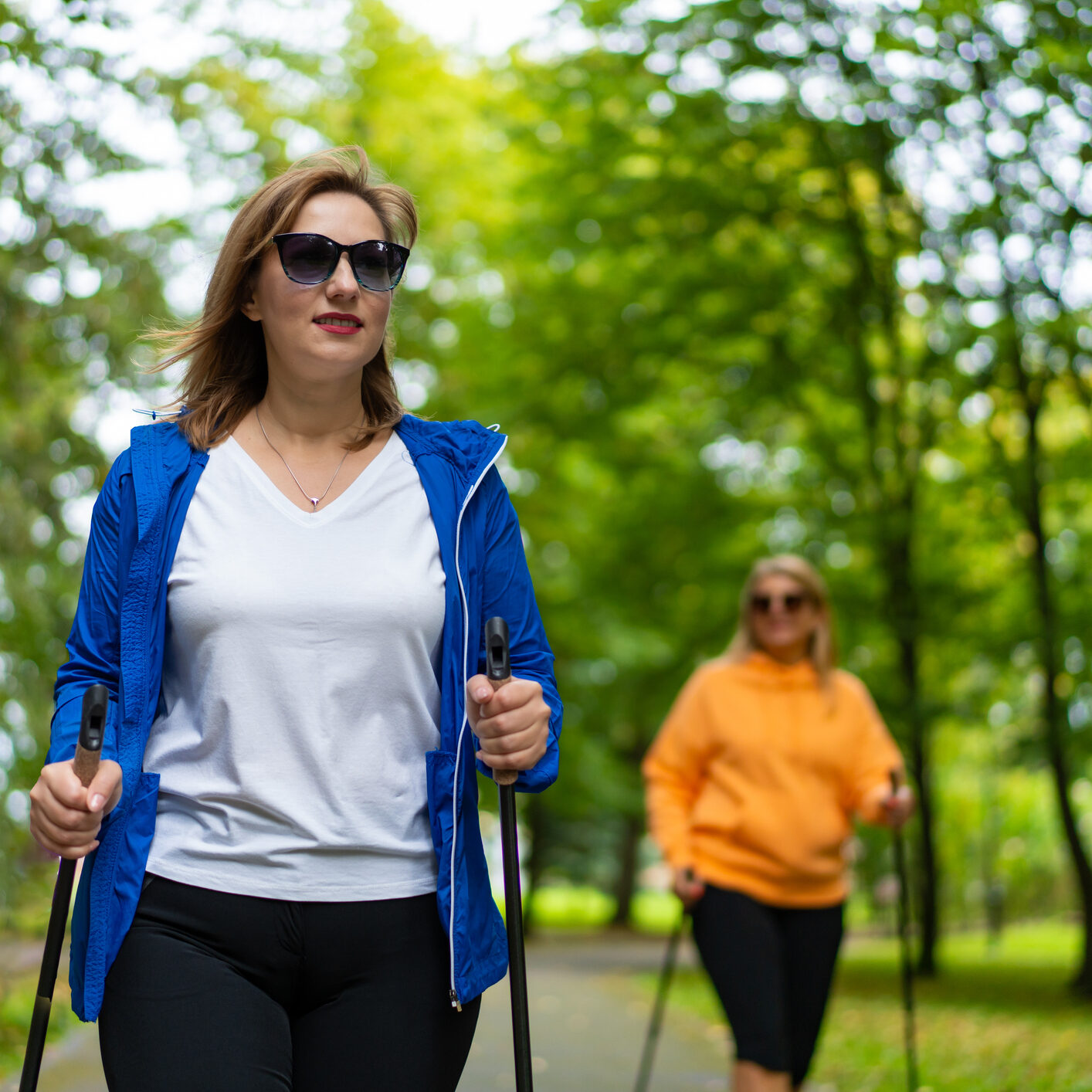 Two pretty mature women practicing Nordic walking in city park. Training of Nordic walking in park. Front view