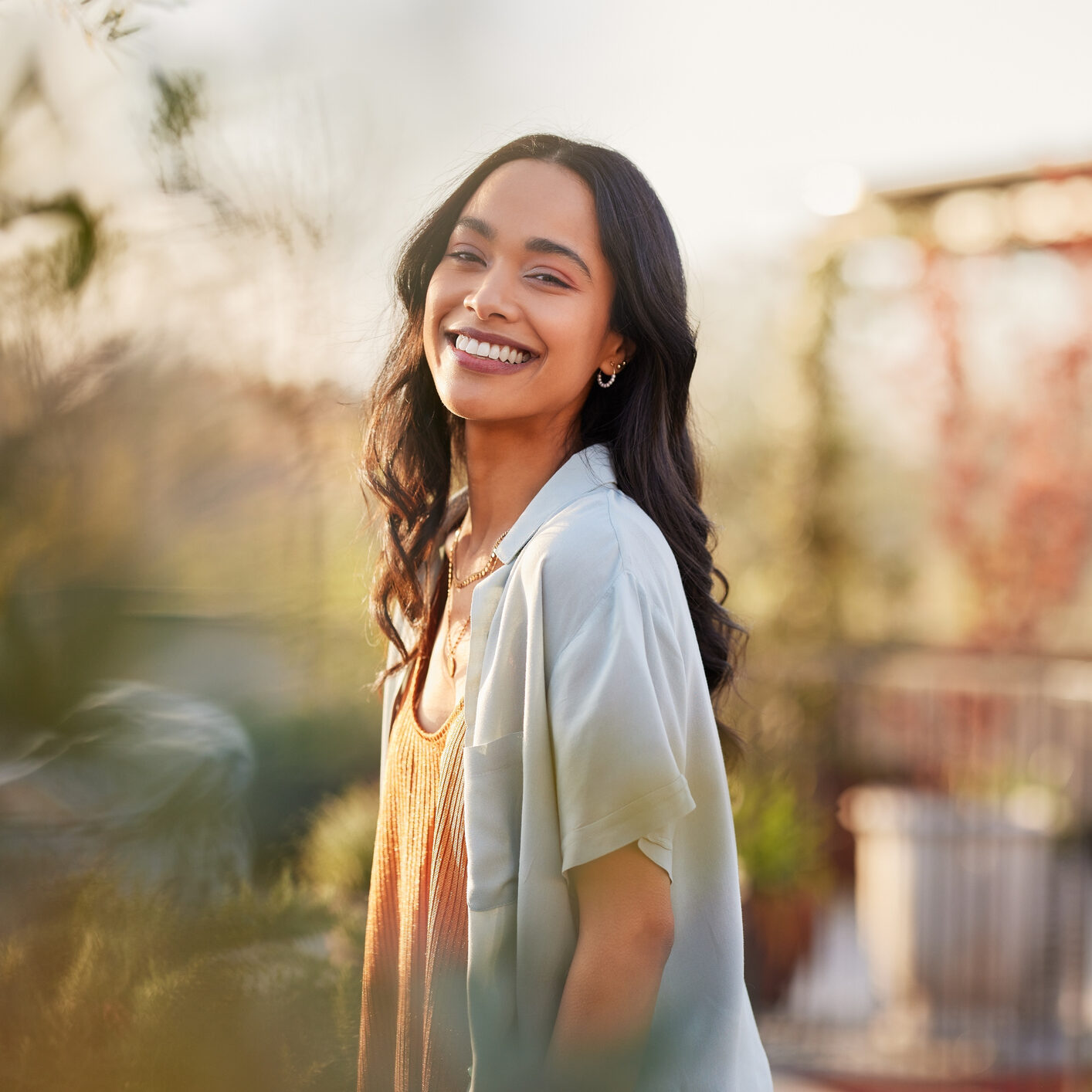 Young latin woman in casual clothing in the garden looking at camera, during early morning. Portrait of healthy mexican girl enjoying nature during sunset. Mindful multiethnic woman enjoy morning ritual with fresh air.